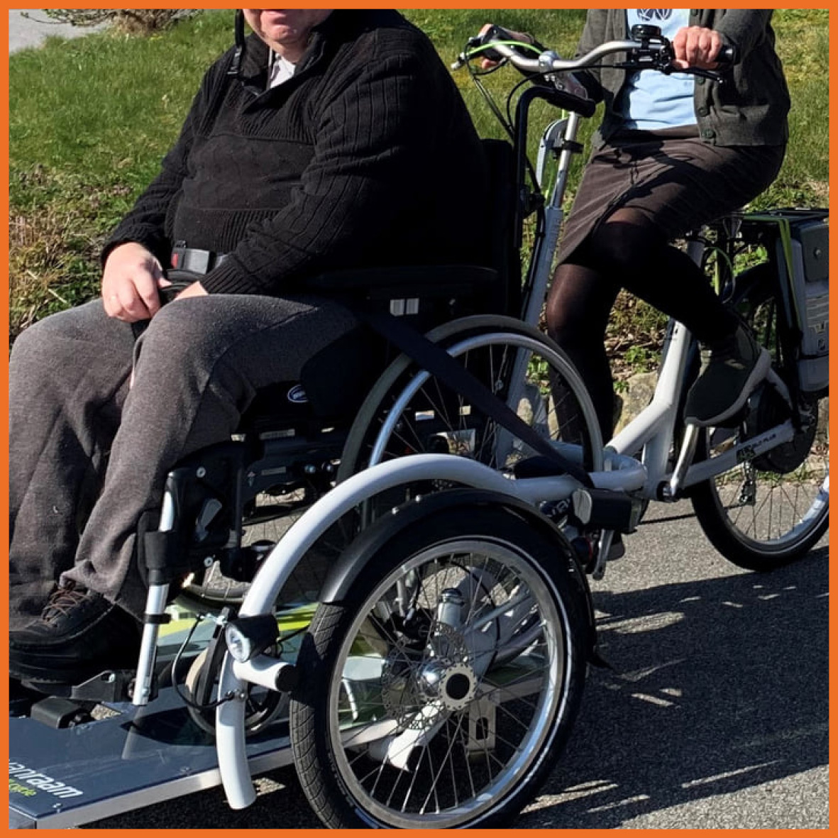 Billede af to personer på en cykel med en kørestol på.